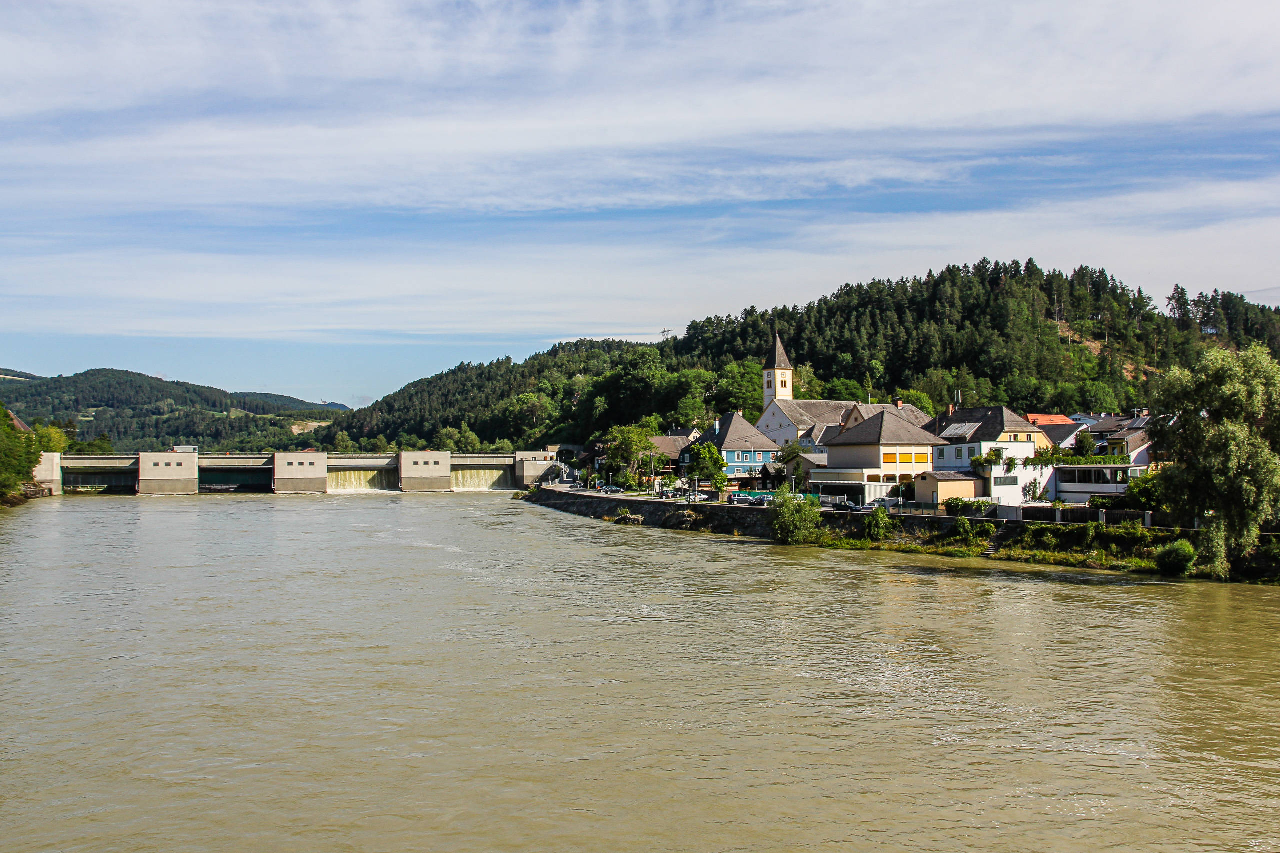 Aufbruch in Lavamünd: Stauwehr an der Drau, dahinter der Ort mit Kirchturm